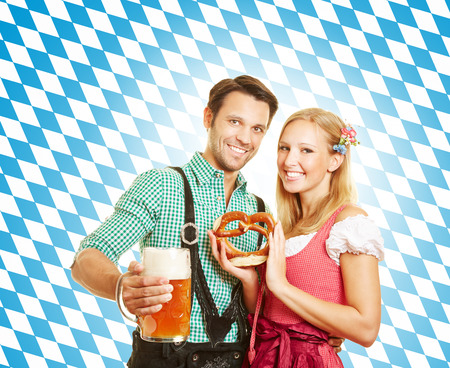 Happy couple celebrating Oktoberfest in Bavaria with beer and pretzelの写真素材