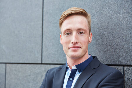 Young smiling business man standing outdoors next to a wall