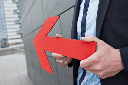 Business man holding red arrow to the left in the cityの写真素材