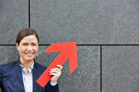 Smiling business woman holding big red arrow upの写真素材