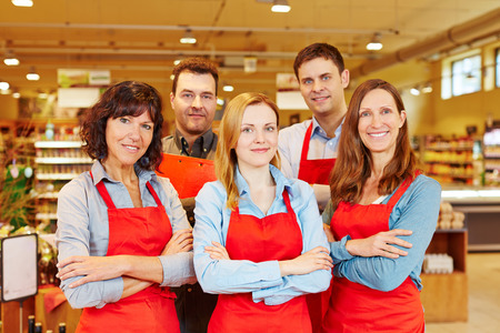 Team of five happy salespeople together in a supermarket with their arms crossedの写真素材