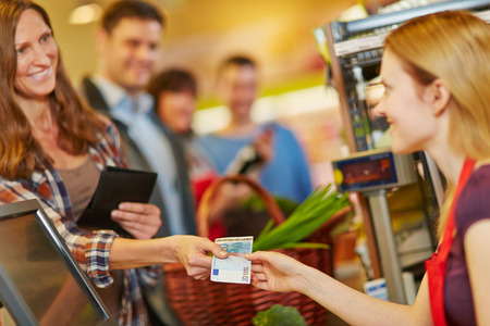 Smiling woman paying with Euro money bill at supermarket checkoutの写真素材