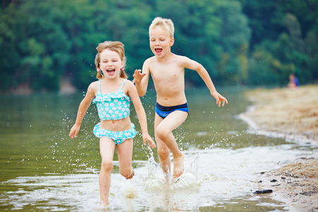 Two happy kids running through sea water in summerの写真素材