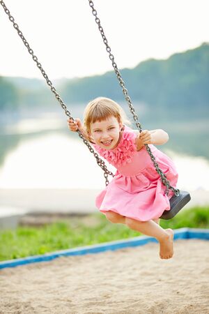 Happy girl swinging on swing in summer on a playgroundの写真素材