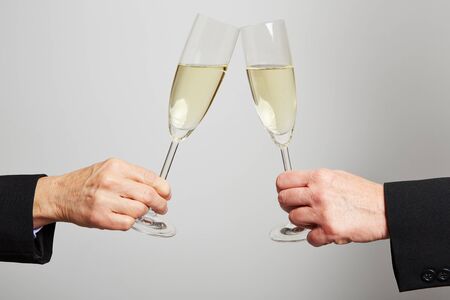 Two old hands clinking champagne glasses for celebrationの写真素材