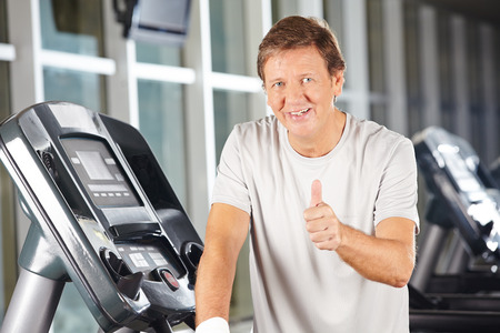Elderly man holding thumbs up in fitness center on a treadmillの写真素材