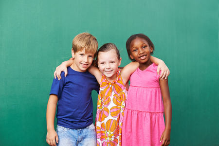 Three happy friends embracing in kindergarten in front of a green wallの写真素材