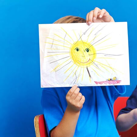Child showing drawing with sun and ocean on a piece of paperの写真素材