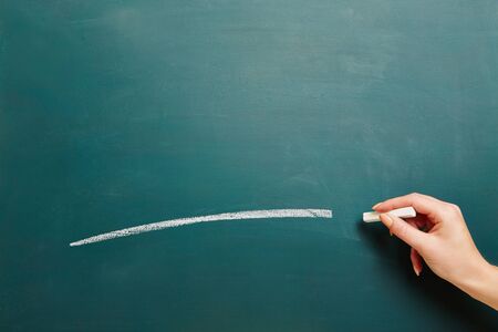 Hand of a teacher drawing white line with chalk on a green chalkboardの写真素材