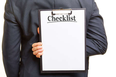 Hand holding a checklist on a clipboard behind his backの写真素材
