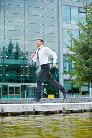 Smiling business man running to appointment in front of office buildingの写真素材