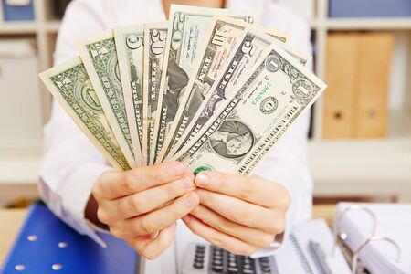 Business woman in her office holding Dollar bill fan