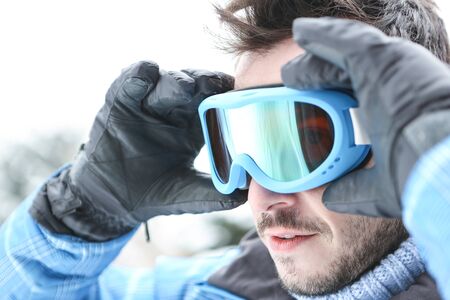 Man on ski trip putting on his ski goggles in winterの写真素材