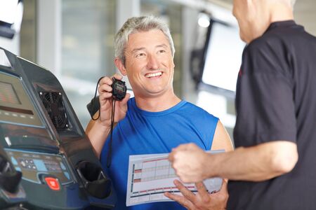Fitness trainer with stopwatch at treadmill with senior man