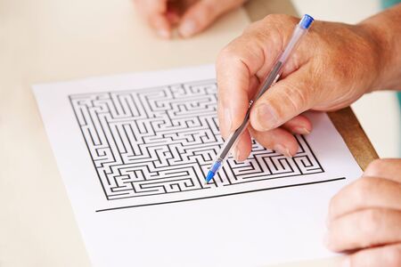 Hand of senior man with pen doing memory training with a paper mazeの写真素材