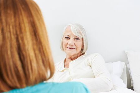 Caregiver talking to bedridden senior woman in her bedの写真素材