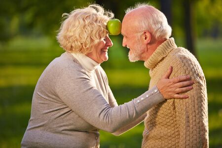 Happy senior caouple balancing apple between forehead in a gardenの写真素材