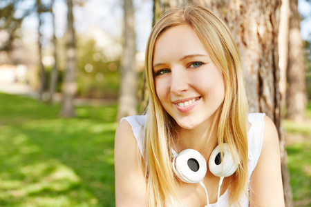 Blonde teenager sitting with headphones in a park in summerの写真素材