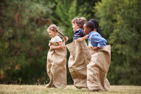Interracial group of kids competing at a sack race in summerの写真素材
