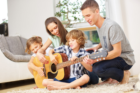 Parents and children playing guitar at home in the living roomの写真素材