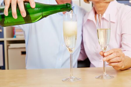 Old couple pouring champagne in glass for New Year's Eveの写真素材