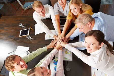 Group of happy business people stacking hands on a desk from aboveの写真素材