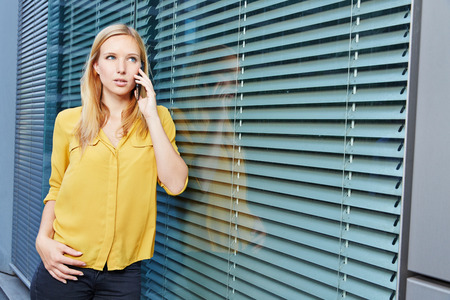 Female blonde student making a phone call with her smartphoneの写真素材