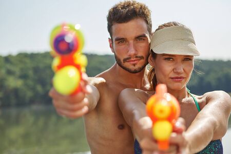 Couple aiming with squirt guns in summer on their holidaysの写真素材