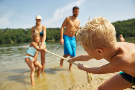 Family and children playing at the lake tug of war on their summer vacationの写真素材