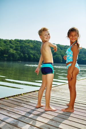 Two children standing on a pier at the lake in summerの写真素材