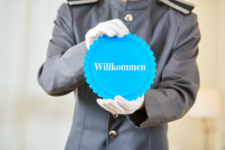 Hotel clerk holding German badge saying "Willkommen" (welcome) in a hotel roomの写真素材