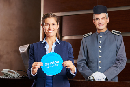 Woman holding service guarantee sign in hotel with smiling concierge behind herの写真素材