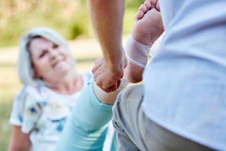 Man gives first aid help to a senior woman with a sprained ankle