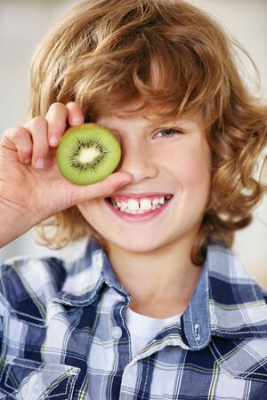 Smiling boy holding kiwi half in front of his eyeの写真素材