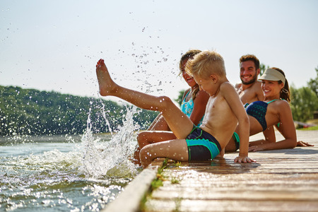 Family bathing and splashing water with their foot at a lake in summerの写真素材