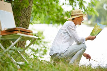 Happy senior woman painting picture in nature in summerの写真素材