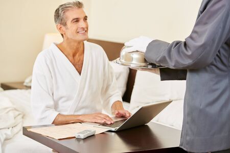 Room service bringing food to a guest with laptop computer in a hotel roomの写真素材