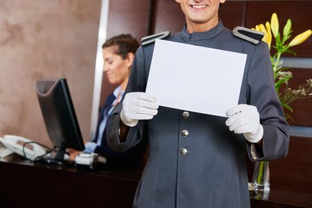 Page in hotel holding empty white blank sign in his handsの写真素材