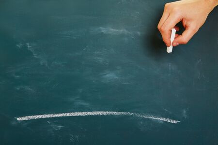Hand with chalk drawing a white line stroke on a green chalkboardの写真素材