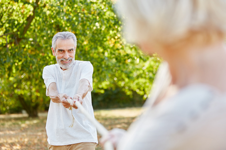 Old man playing tug of war with his wife in summer in the natureの写真素材