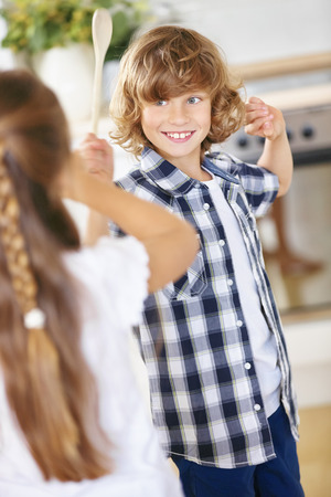 Boy and girl fighting in jest with wooden spoons in a kitchenの写真素材