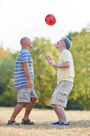 Two seniors having fun during a soccer match in the park in summerの写真素材