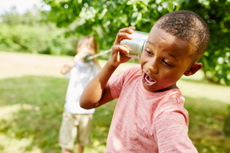 African boy calling friend with tin can telephone in summer in the parkの写真素材