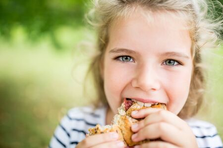 Blond child eats bun as a snack in summerの写真素材