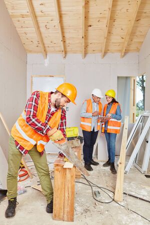 Carpenter cutting wood while artisans plan renovationの写真素材