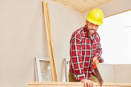 Craftsman holding saw and cutting wood at construction site