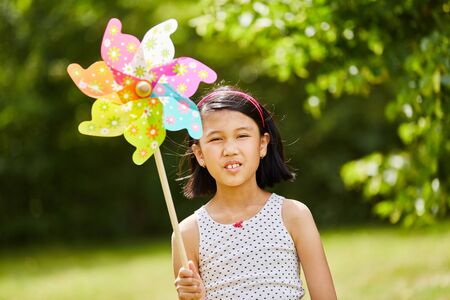 Asian child playing with windmill in the park in autumnの写真素材