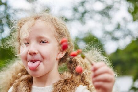 Girl stretches naughty tongue out while rosehip picking in autumnの写真素材