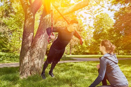 Personal trainer with man at the park fitness training with sling