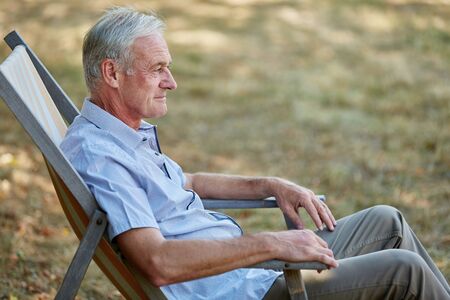 Old man sitting relaxed on a deck chair in summer in the nature